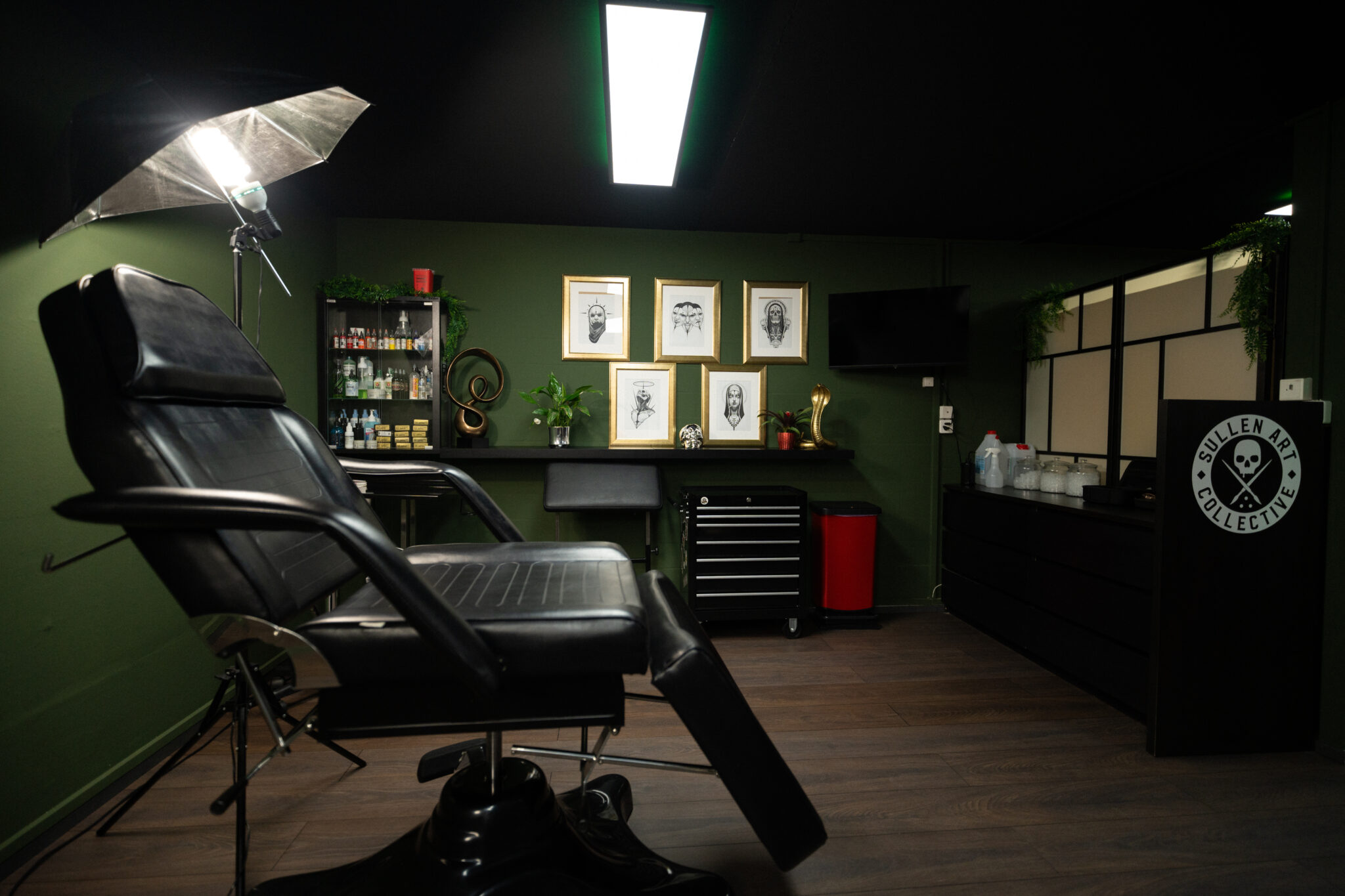 Arbeitsplatz im Tattoo-Raum mit Farben, Werkzeugwagen und gerahmten Zeichnungen